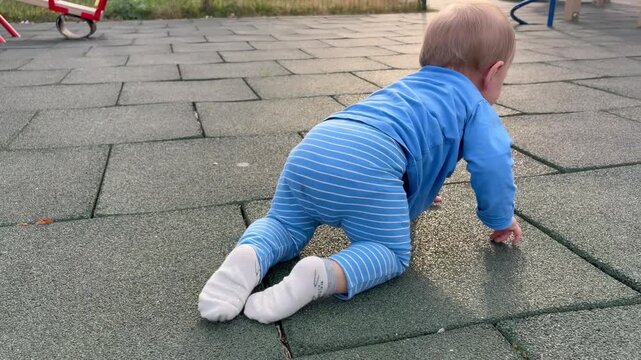 a boy under one year old crawling on his knees on the playground surface. The child's early motor development