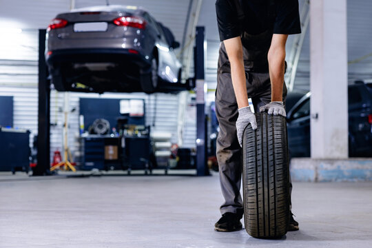 Mechanic rolling tire across garage floor near lifted vehicle, service for change of wheels