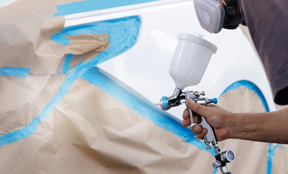 Person spraying paint on vehicle panel in automotive workshop