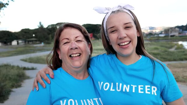 Happy multigenerational volunteers hugging and laughing outdoors in city park wearing matching blue t-shirts - Family bonding and community service concept
