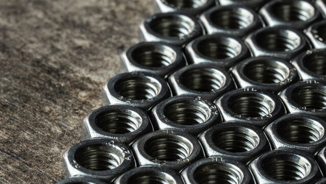 Group of metallic hex nuts creating a textured pattern, representing industrial strength and connection on a concrete surface