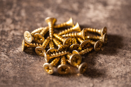 Golden screws forming pile on rough gray surface, representing fasteners, construction, and diy hardware