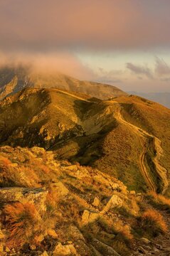 Beautiful autumn evening landscape of Western Tatras mountain ridge with hiking trail in golden sunset light, scenic view of hills and glowing low clouds in Tatra National Park, Slovakia.