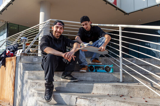 Two young men sitting on concrete stairs with a skateboard and boombox, representing youth culture