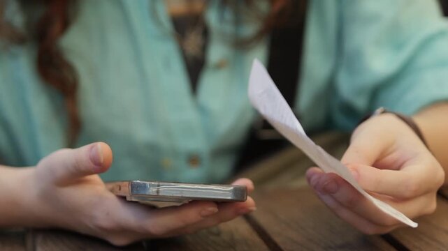 Cinematic close-up girl checking a cafe receipt while using a smartphone at a wooden table. Perfect for finance, budgeting, restaurant payment, consumer spending, digital banking, lifestyle, and mobil