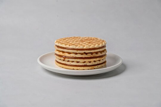 Stack of Stroopwafel, thin waffles with caramel syrup filling, neatly arranged on white plate. Concept of simplicity, highlighting thin waffles with caramel syrup filling.