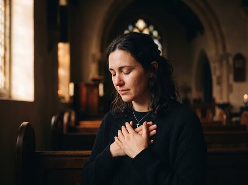 Young woman with hands on chest praying inside a dimly lit church interior