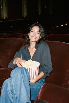 Cheerful woman with popcorn seated in a dark theater for film night banner and cinema entertainment background design