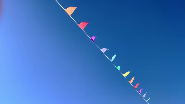 Long line of colorful pennant flags waves high across cloudless blue sky