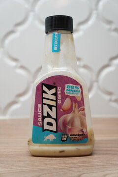 A bottle of Dzik garlic sauce with low fat content displayed on a wooden kitchen countertop surface