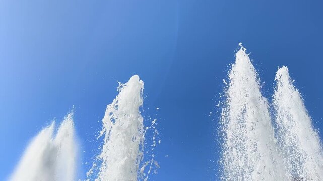 Multiple fountain jets spray upward and shimmer against a cloudless blue sky