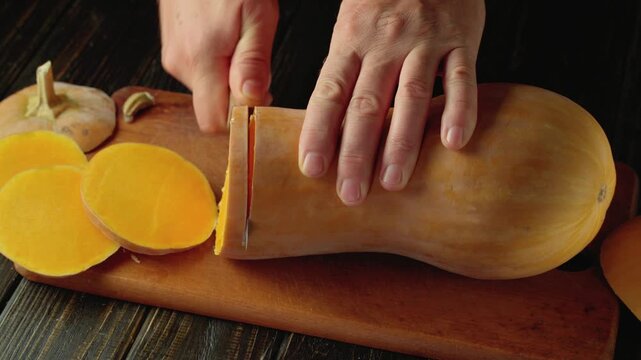 Hand slicing butternut squash into even rounds on a wooden cutting board, with vibrant orange flesh and smooth skin visible alongside discarded pieces in a well-lit kitchen setting