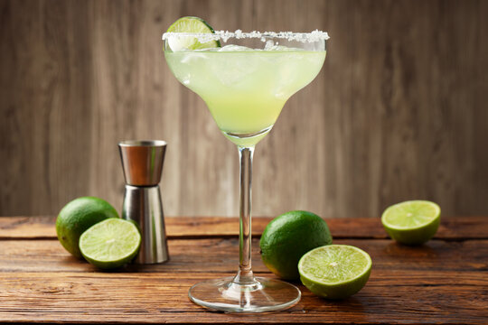 Refreshing margarita cocktail in glass, limes and jigger on wooden table, closeup