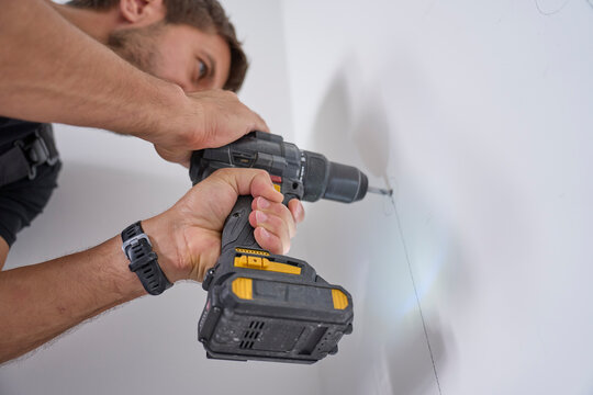 Man drills hole in white interior wall with cordless power drill