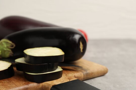 Fresh raw eggplants, board and knife on light grey table, closeup. Space for text