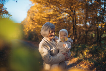 Grandmother kissing baby outdoors in autumn nature.