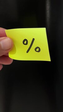 Hand holding percentage discount sticky note vertical black background