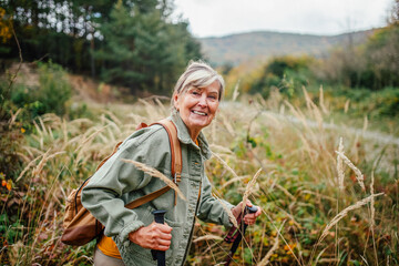 Fototapeta premium Happy senior woman on nature walk during rainy autumn day.