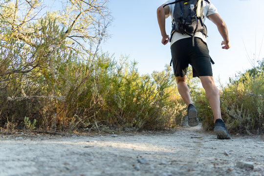 Athlete wearing backpack running on a dirt trail surrounded by nature. Pursuing fitness goals and active lifestyle