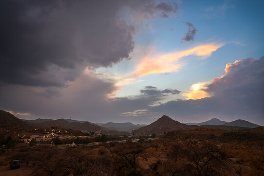 Saudi Arabia Tourism - Scenic sunset sky with golden clouds and storm clouds over Al Taif mountain landscape and desert resort lights, ideal for Saudi National Day and travel campaigns
