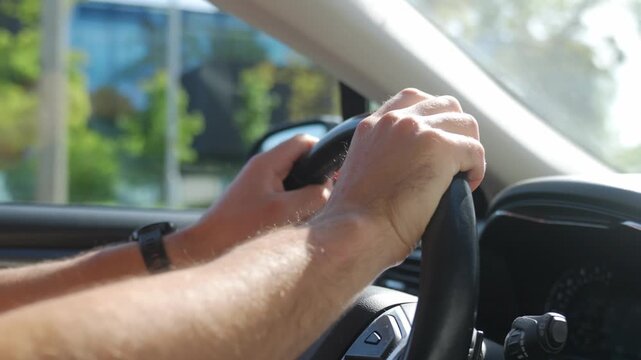 Man holds steering wheel with both hands while driving car in daylight. Close view of driver control and road safety