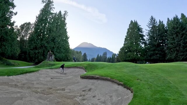 man hit golf bunker shot with beautiful mountain backdrop