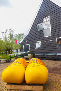 Giant yellow traditional wooden clogs on the pavement near an authentic Dutch house facade in Zaanse Schans, Zaandam, Netherlands
