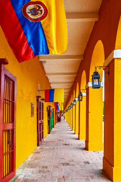 Historic yellow arches of Las B&oacute;vedas in Cartagena, Colombia, featuring vibrant Colombian flags, colonial architecture, and a long brick corridor with vintage lanterns.