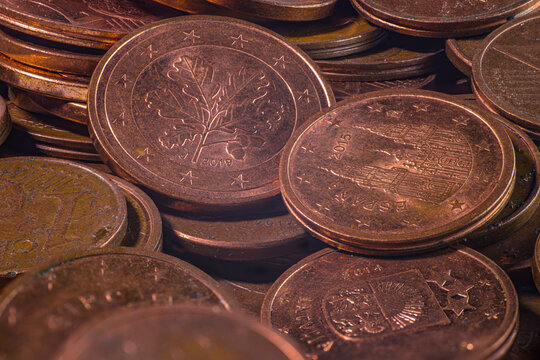 Closeup of overlapping copper colored euro cent coins showing embossed national designs, stars, numbers, worn metallic surfaces, and detailed circular edges in a coin pile