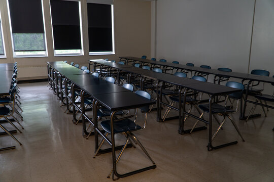 Empty modern classroom or training room setup with neat rows of black tables and blue folding chairs, windows with pulled blinds, ideal for education, corporate training, or event concepts.