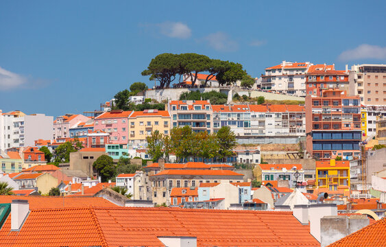 Residential buildings and traditional red tiled roofs cover a sunny hillside in Lisbon, Portugal.