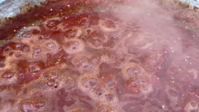 Close-up of homemade tomato sauce boiling in a large pot, showing rich red texture, bubbles and tomato seeds during traditional slow cooking and food preservation.