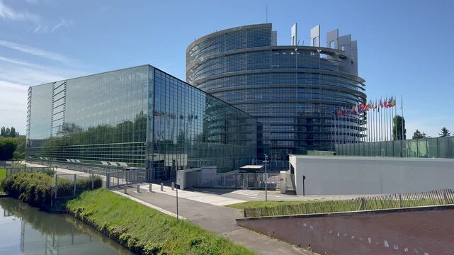 View of the European Parliament building in Strasbourg, France, featuring modern glass architecture and European flags under a clear blue sky.