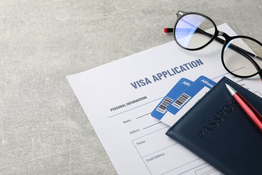 Visa application form, passport with tickets, pen and glasses on grey table, closeup. Space for text