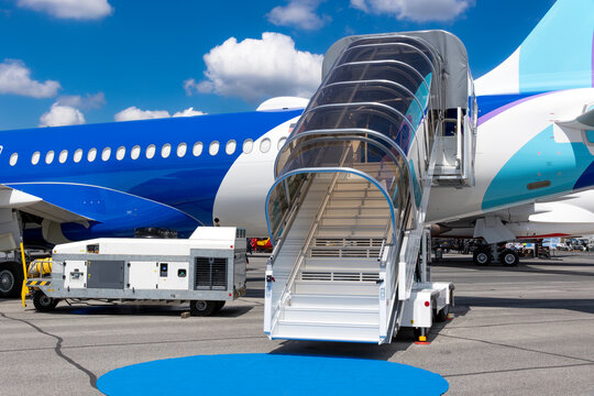 Mobile airstairs parked against a passenger aircraft on an airport apron, providing access to the aircraft cabin.