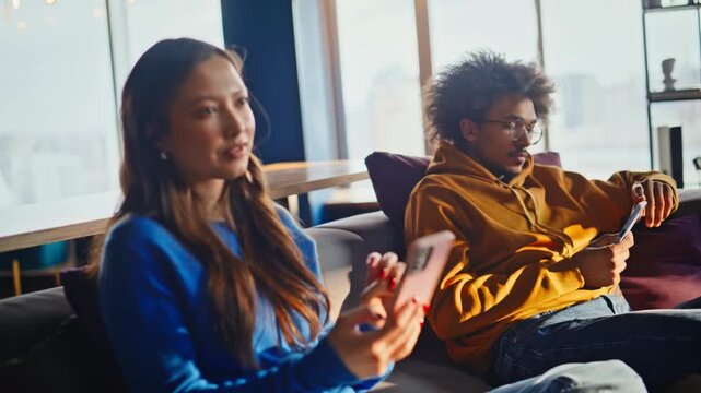 Diverse coworkers browsing phones back to office lounge. Team break sofa.
