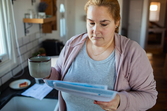Woman reading household bills with coffee in kitchen