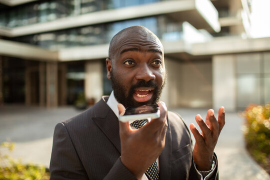 Businessman using smartphone voice command outside a modern office