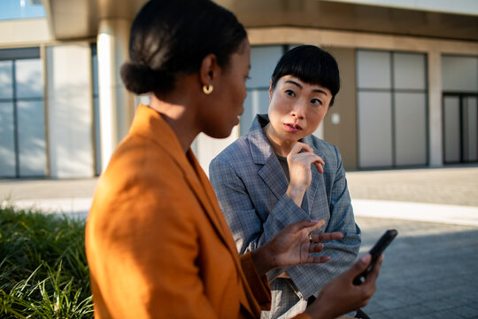 Two businesswomen discussing strategy on smartphone outside office