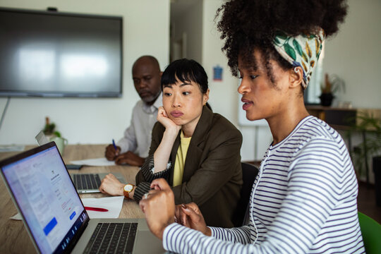 Colleagues collaborating on laptop during team meeting in modern office