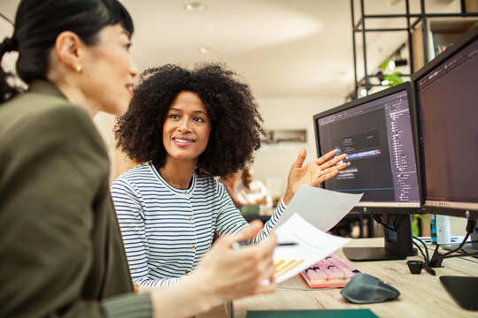 Two female colleagues collaborating on software design at computer in modern office