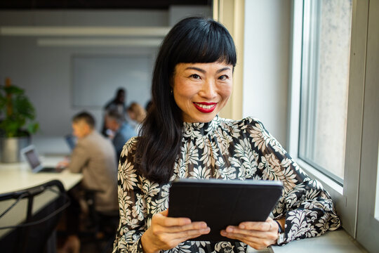 Smiling businesswoman holding tablet by office window