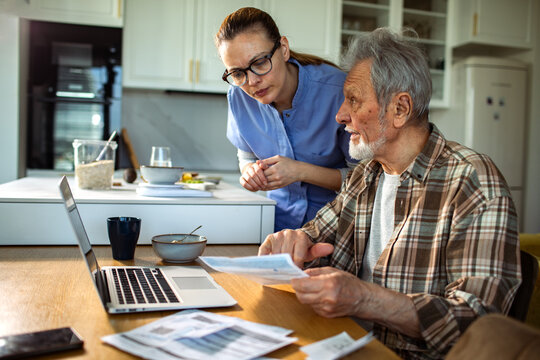 Home caregiver helping senior man review finances at kitchen table