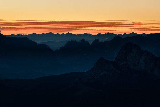 Layered mountain ridges of the Italian Dolomites fade into atmospheric haze beneath a glowing sunset horizon, creating a dramatic landscape for hiking, trekking and alpine travel themes.
