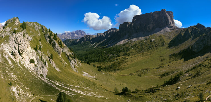 Panoramic view across the green Mondeval alpine basin toward the massive rock walls of Lastoi de Formin near Passo Giau in the Italian Dolomites. Colors: green, gray, blue