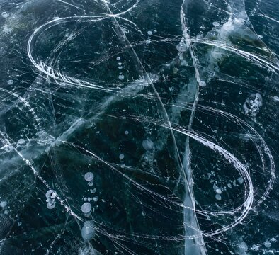 Frozen lake surface marked with skate trails and scuffed white arcs across dark clear ice