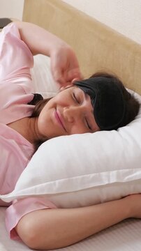 Beautiful woman in pink pajamas and a sleep mask waking up in a cozy bed, smiling and stretching as she enjoys a peaceful morning, feeling well rested and ready for the new day