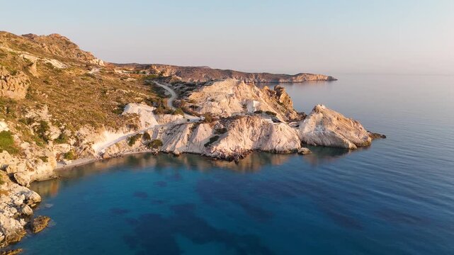 Early morning sunlight during a beautiful sunrise over the Aegean sea seen from the shore of Mandrakia on the Greek island Milos in Greece. Unique landscape on the coastline, natural blue ocean water