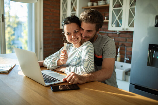 Happy couple celebrating positive pregnancy test at home kitchen
