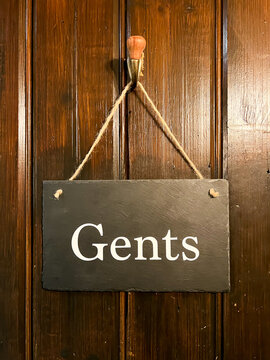 A slate door string hanging via string and a hook on the back a of a gent's toilet door